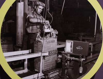 Historical image of early asbestos bagging operation, using mechanical zip-sewing equipment.